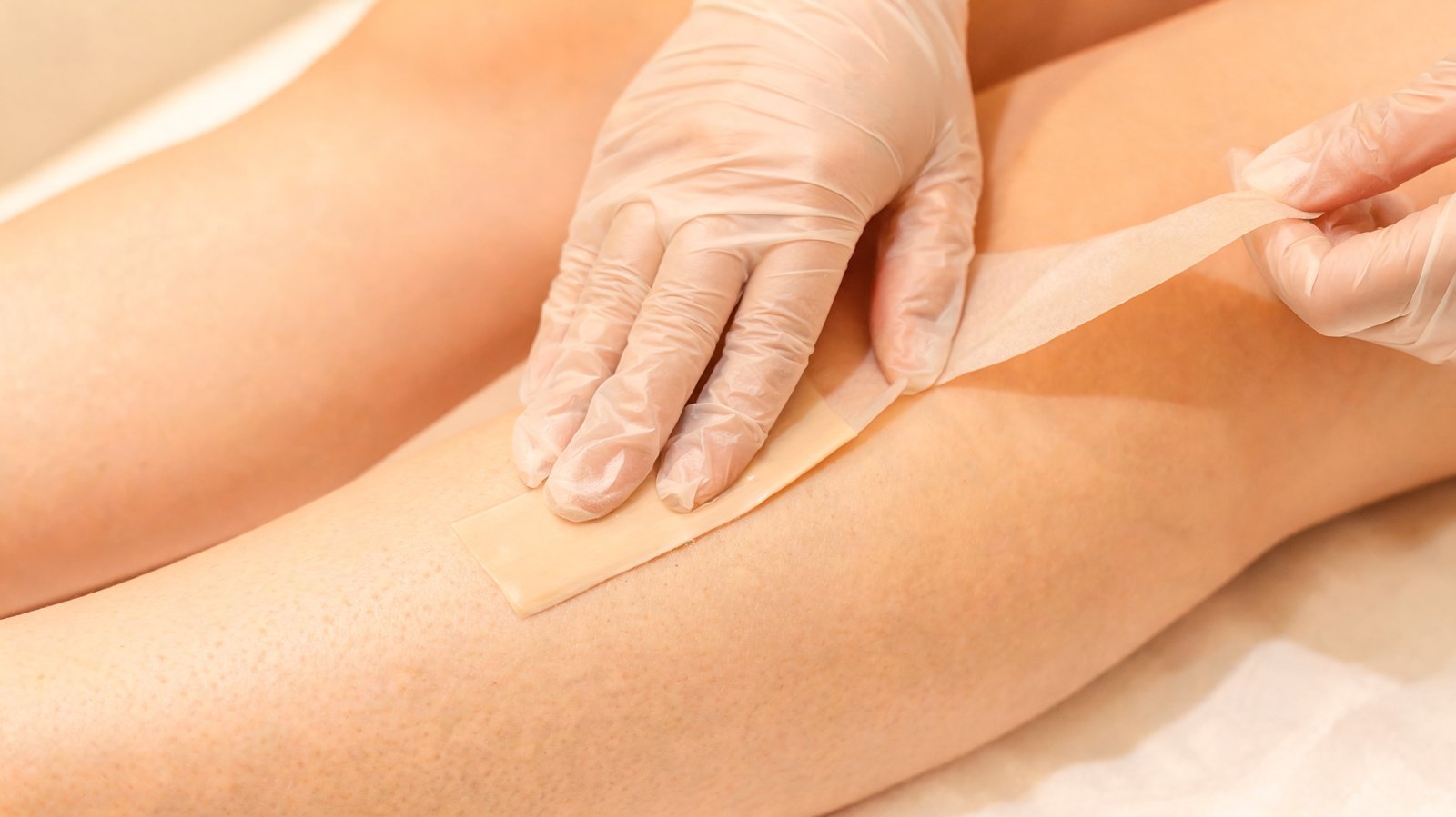 Wax strip being applied to client's lower leg by esthetician